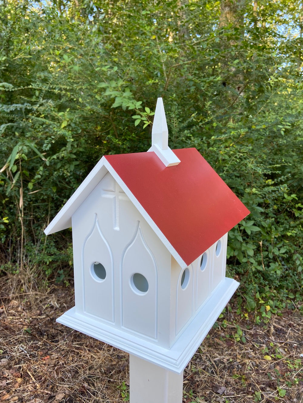 Merlot chapel birdhouse on white post with woods in the background