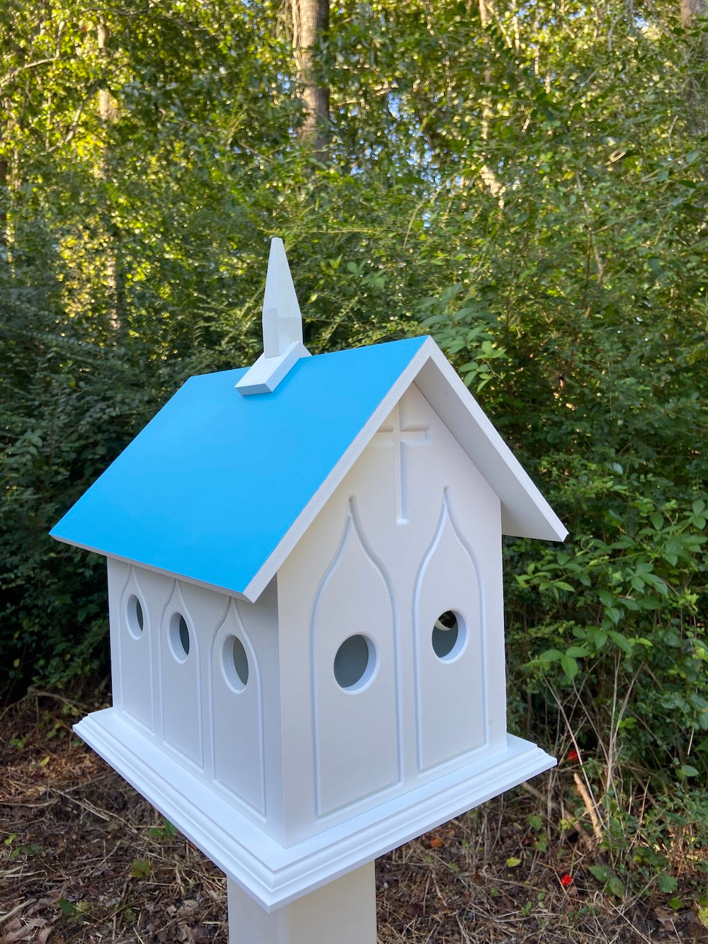 Lagoon blue chapel birdhouse on white post with woods in the background