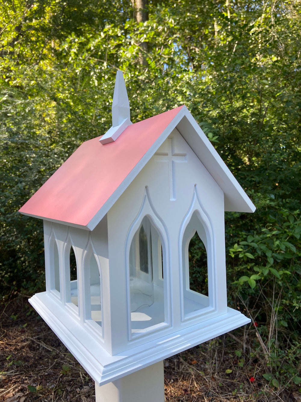 Coral isle chapel bird feeder mounted on white post with woods in the background