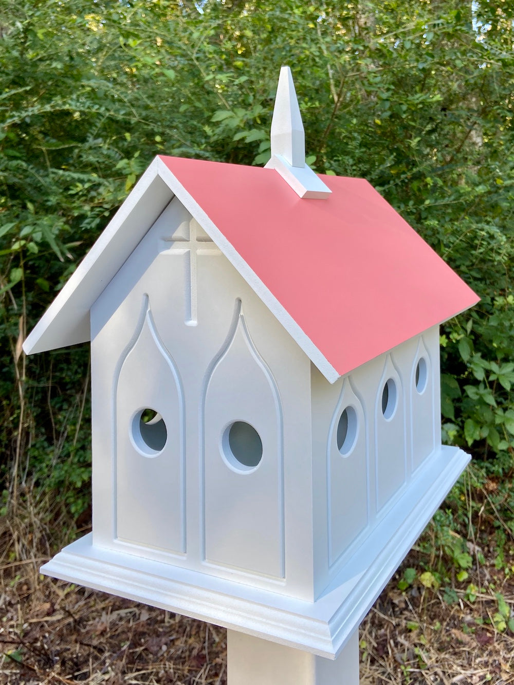 Coral isle chapel birdhouse on white post with woods in the background