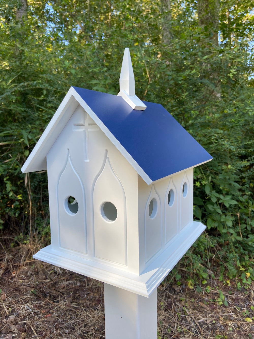 Cobalt blue chapel birdhouse on white post with woods in the background