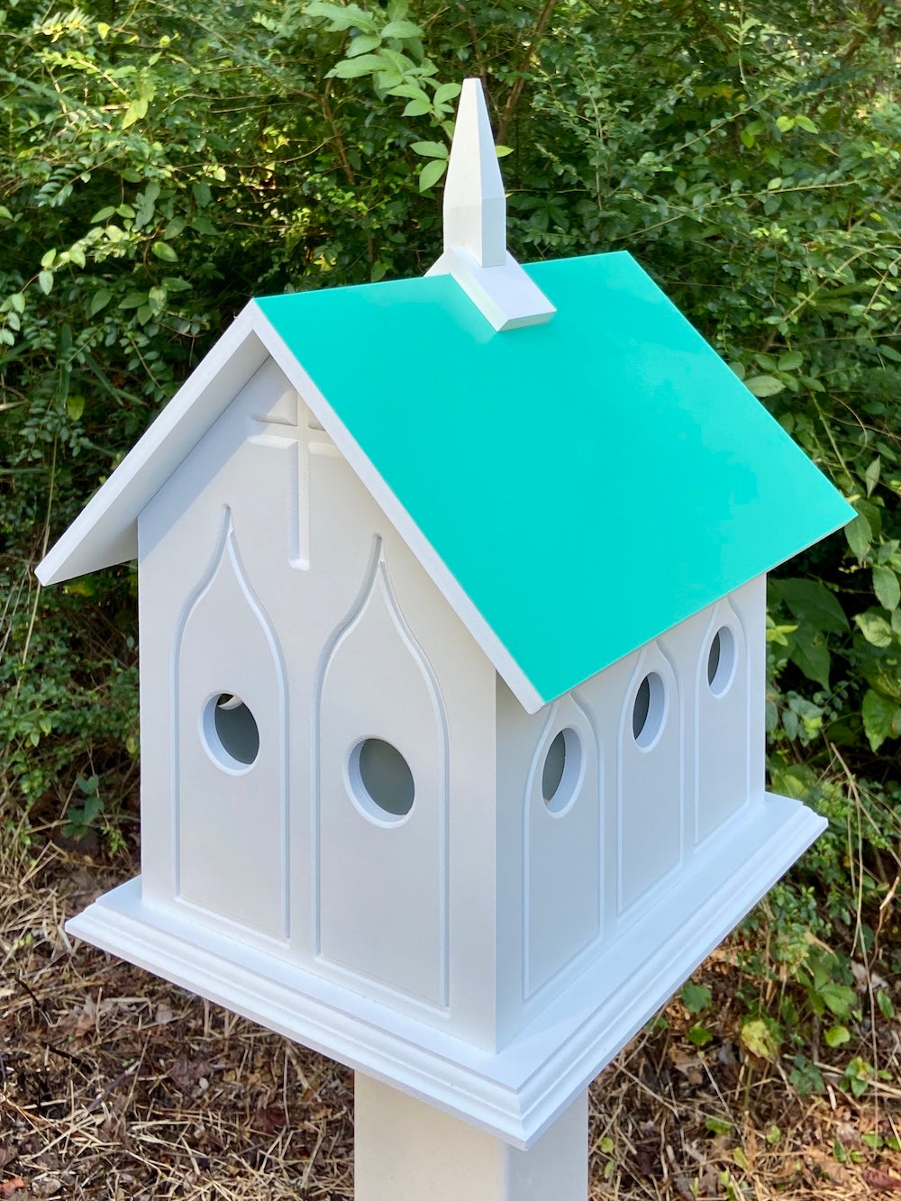 Beach glass chapel birdhouse on white post with woods in the background