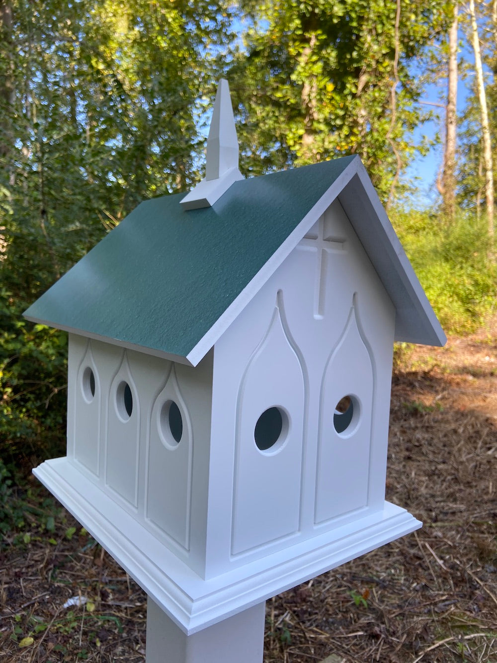 Verde chapel birdhouse on white post with woods in the background