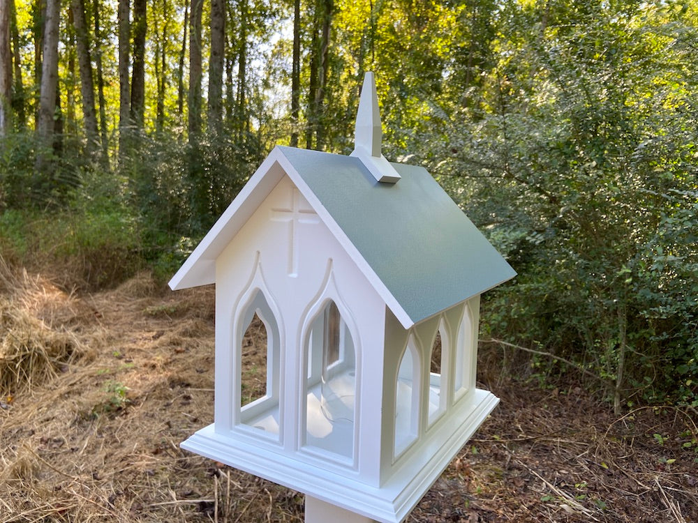 Verde chapel bird feeder mounted on white post with woods in the background