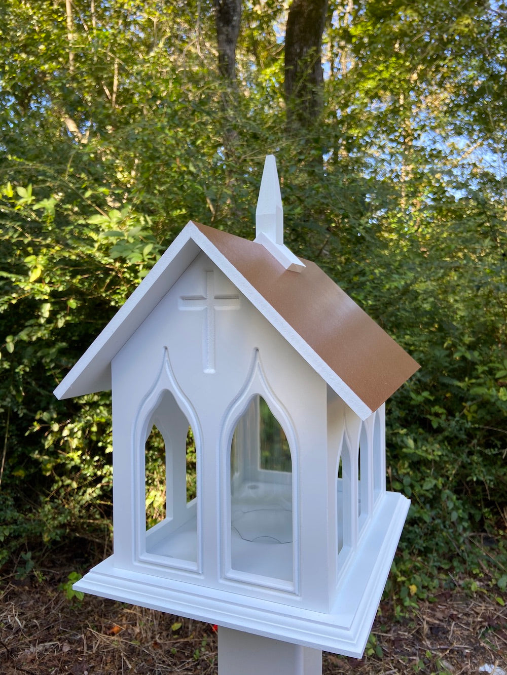 Hammer copper chapel bird feeder mounted on white post with the woods in the background