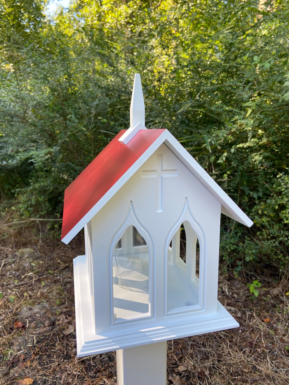 Merlot chapel bird feeder mounted on white post with the woods in the background