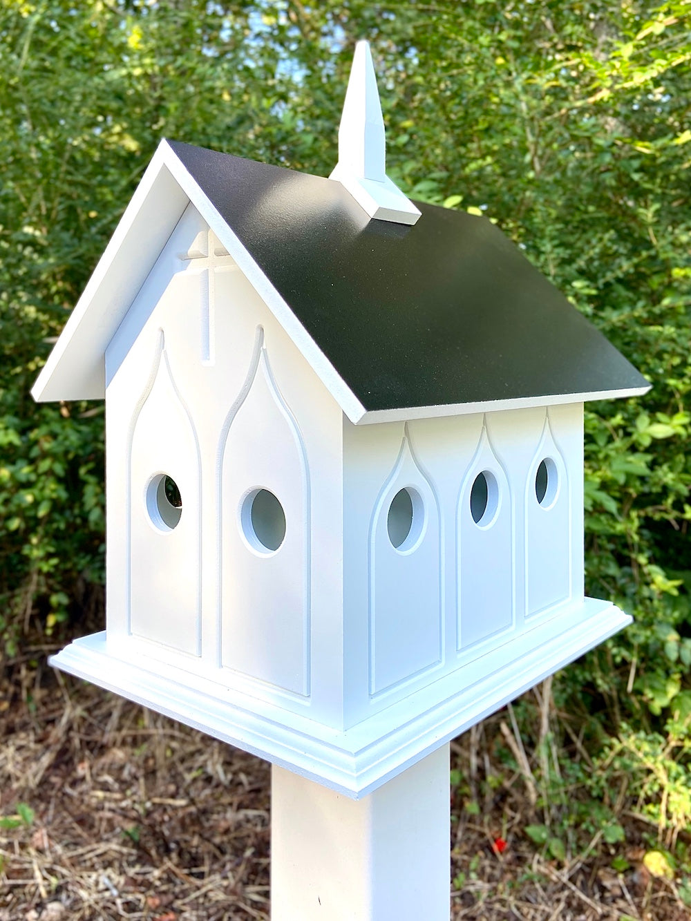 Black chapel birdhouse on white post with woods in the background