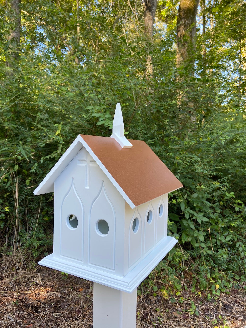 Hammer copper chapel birdhouse on white post with woods in the background