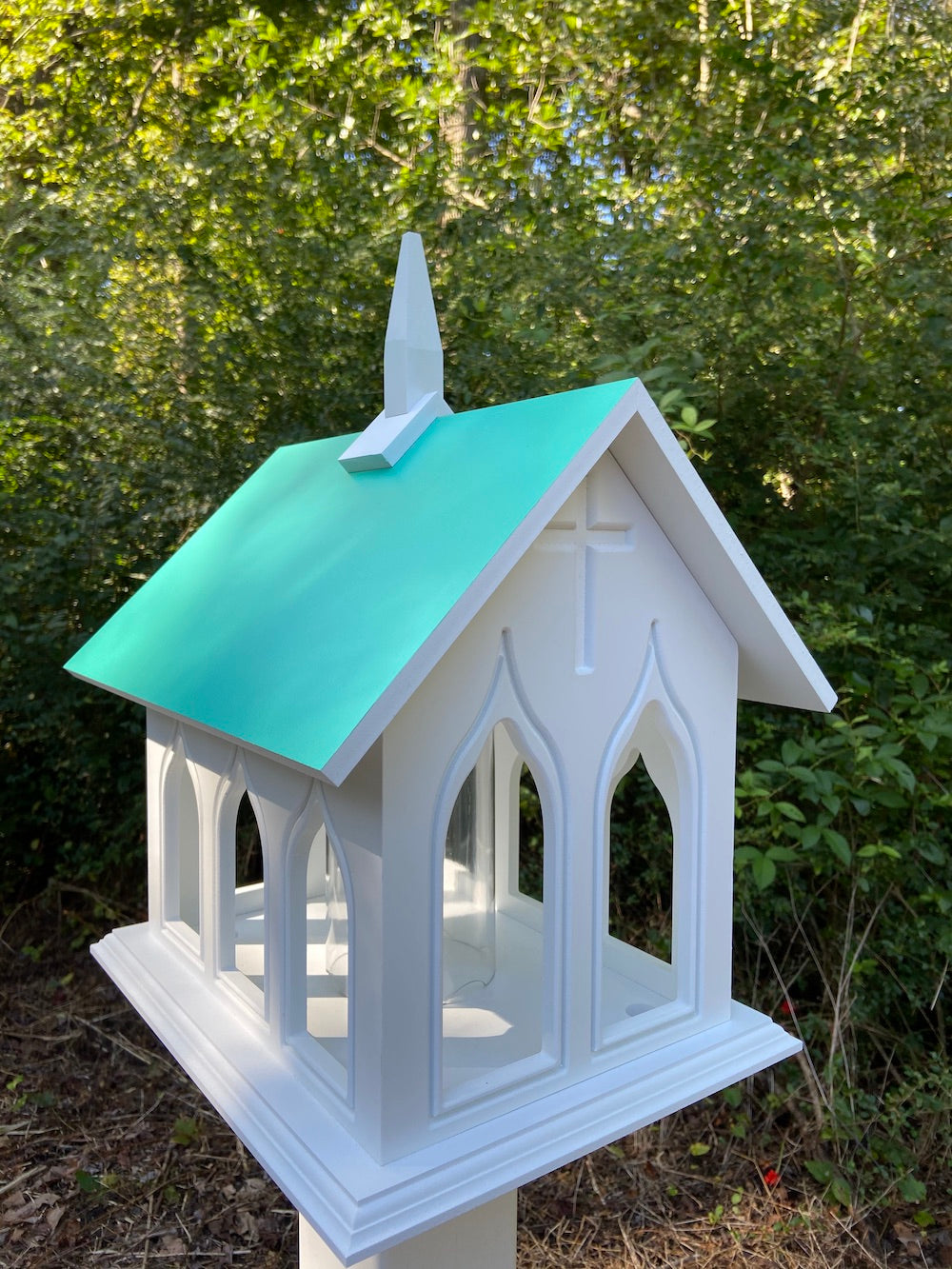 Beach glass chapel bird feeder mounted on a white post with the woods in the background